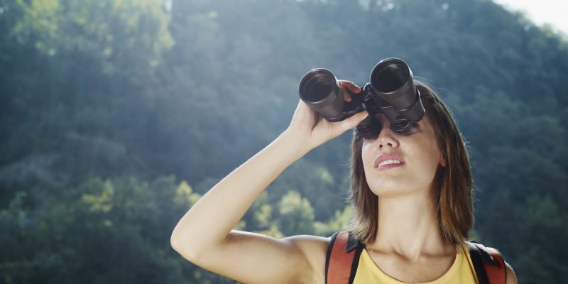 Young Woman Hiking On Mountain With Binoculars